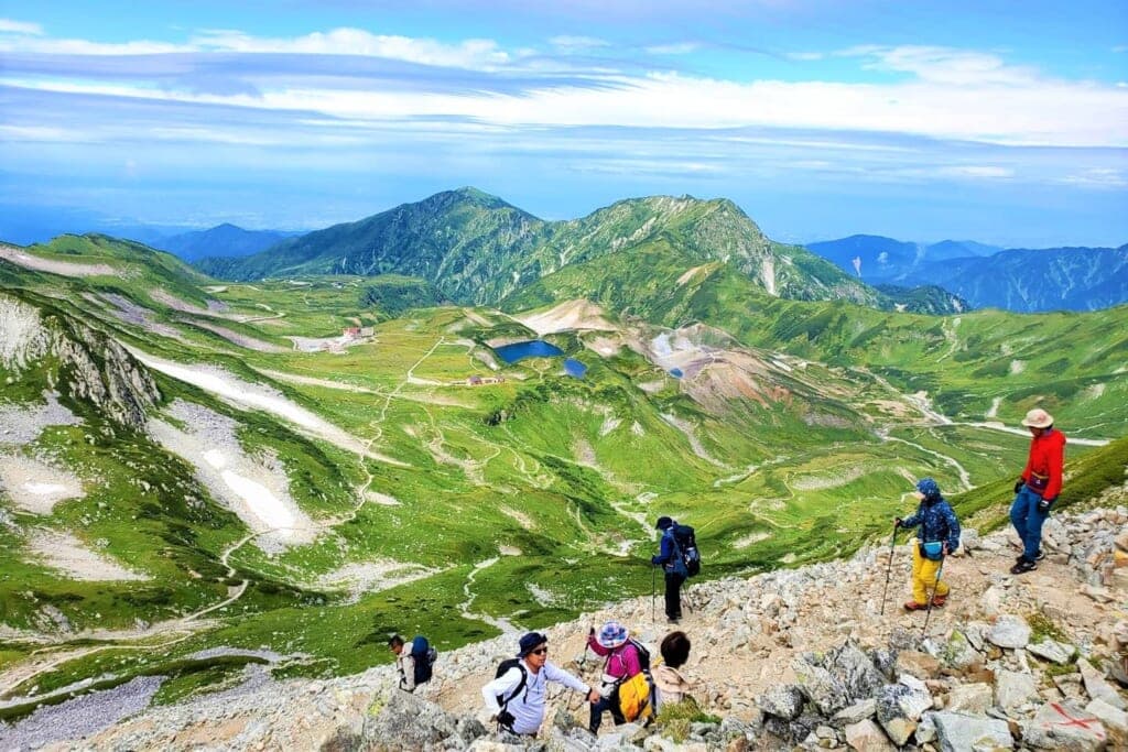 Trilheiros na crista de Tateyama com o vale alpino verde ao fundo